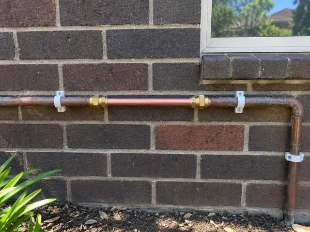 Repaired copper water pipe on a brick house wall below a window in Forestville