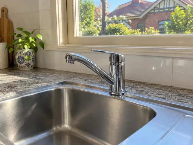 Chrome kitchen mixer tap above a stainless steel sink and stone-look bench by a window in Lindfield